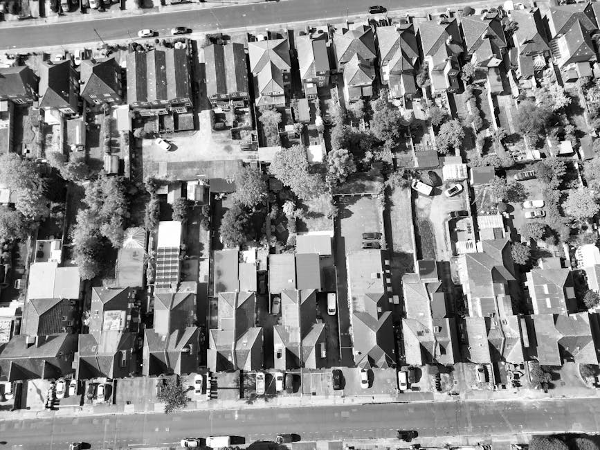 A black-and-white aerial photograph of a residential neighbourhood showing a row of terraced houses with pitched roofs along a tree-lined street. The area features a variety of detached and semi-detac